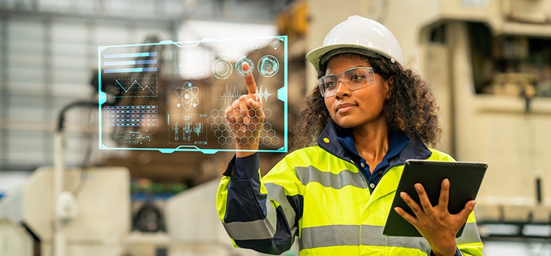 Woman wearing vest and hardhat looking at a digitized computer screen 